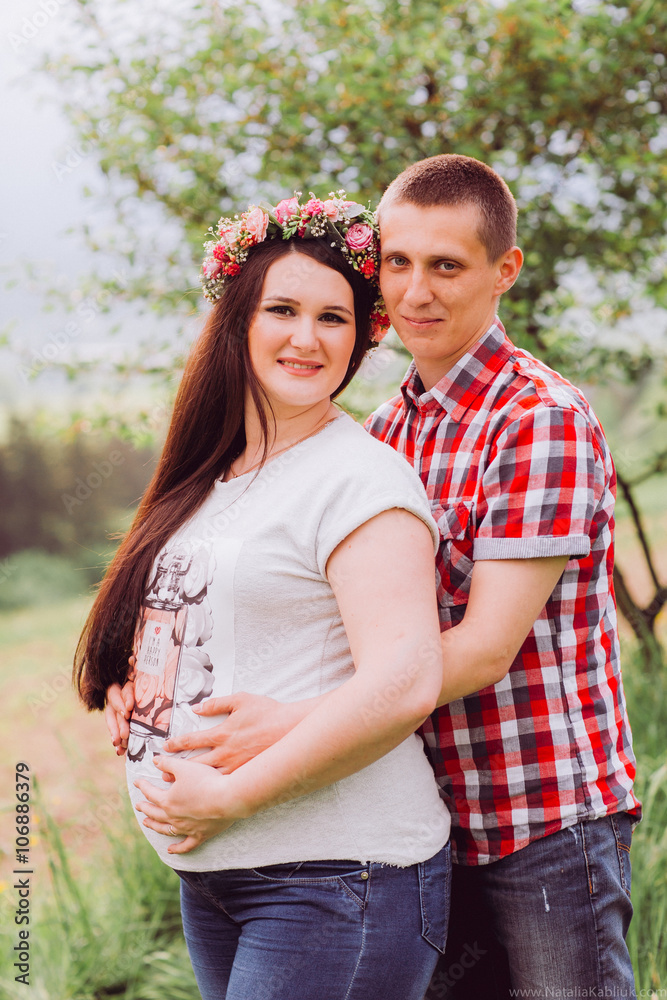 Fototapeta premium Pregnant woman in blue jeans and a T-shirt with her husband on the mountains background. Future parents