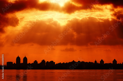 City silhouette and red sky with sun rays