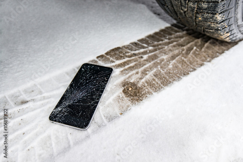 Fototapeta Naklejka Na Ścianę i Meble -  Phone with broken screen on snow in car trails