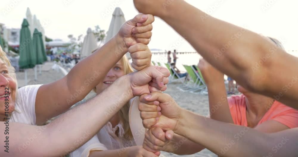 Tilt shot of people sitting at wooden table on the beach and stacking fists in a tower. Teamwork and cooperation