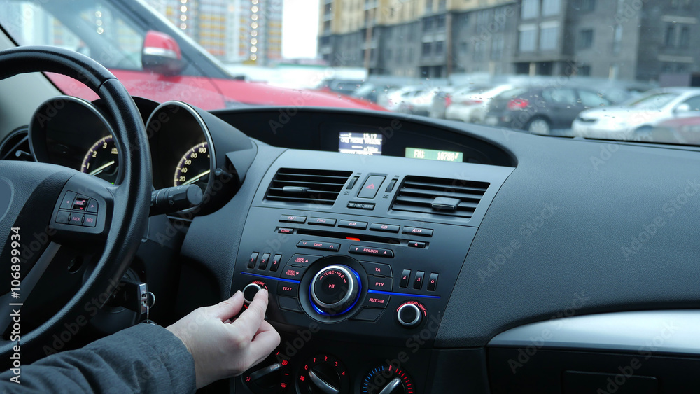 Мужчина настраивает радио автомагнитолы и регулирует громкость в автомобиле