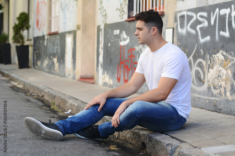 Young latin man sitting at the street