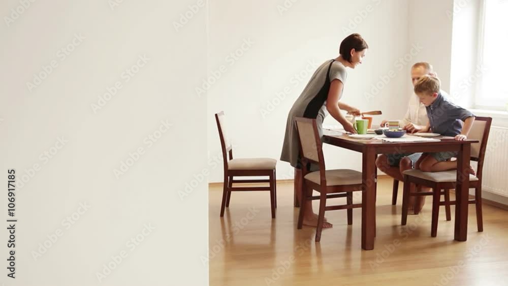Family gathers at the table for breakfast: mother is serving food Family gathers at the table for breakfast: mother is serving food
