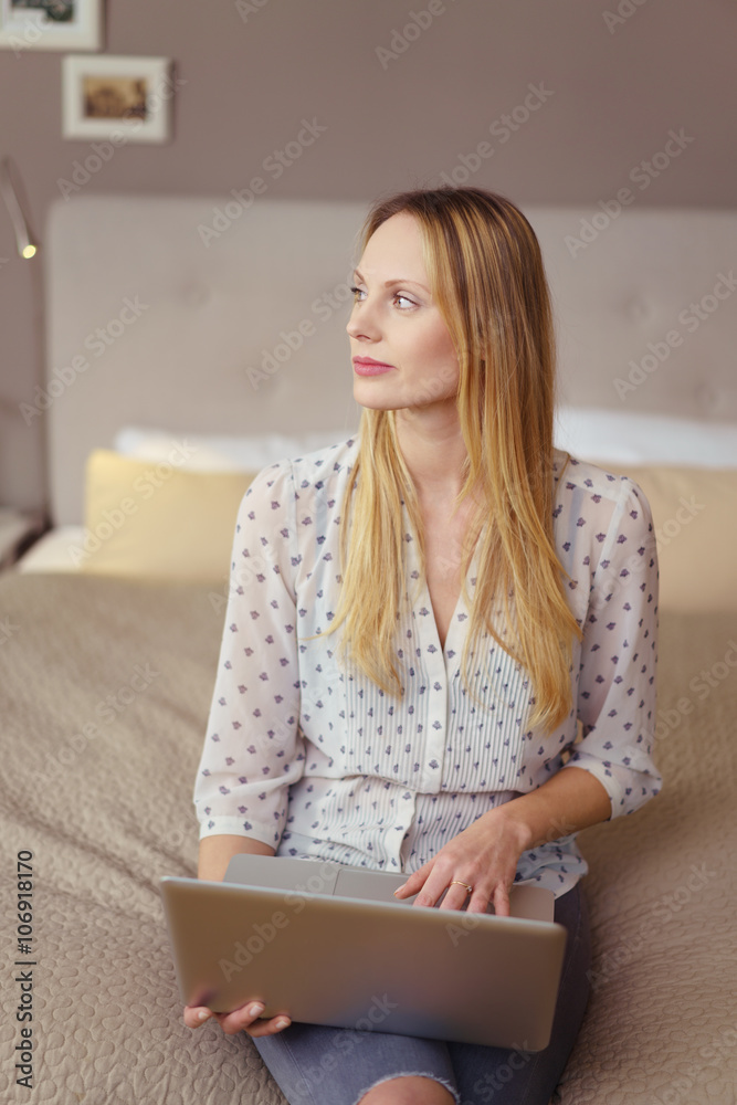 frau sitzt mit laptop auf dem bett und schaut nachdenklich zur seite frau sitzt mit laptop auf dem bett und schaut nachdenklich zur seite