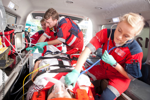 Paramedics using stethoscope on patient in ambulance photo