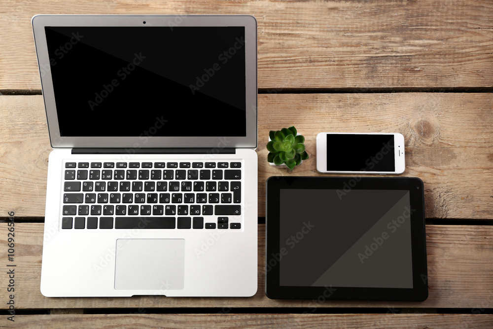Different modern devices with green plant on wooden table Different modern devices with green plant on wooden table
