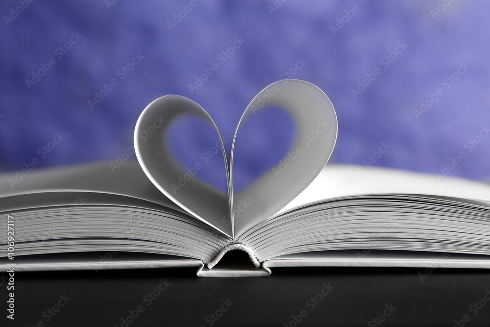 Sheets of book curved into heart shape on unfocused blue background Sheets of book curved into heart shape on unfocused blue background