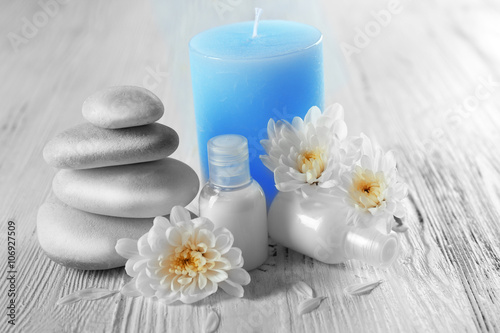 Spa wellness with stacked zen stones, blue candle, white flowers, and lotion bottles on rustic wood