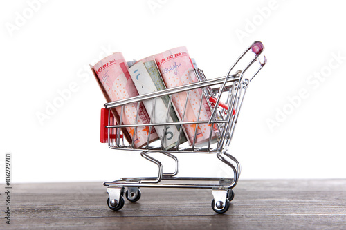 Small shopping trolley with euros banknotes on wooden table isolated on white