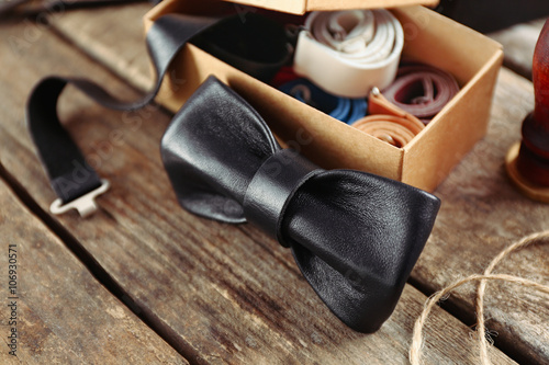 Black bow tie and full cardboard gift box of ties on wooden table, close up photo