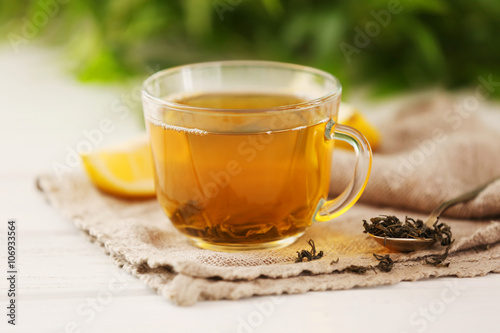 Glass cup of green tea with sliced lemon on wooden table with sackcloth closeup