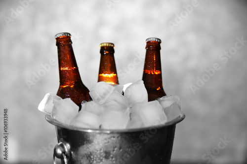 Brown glass bottles of beer in ice-pail on grey background