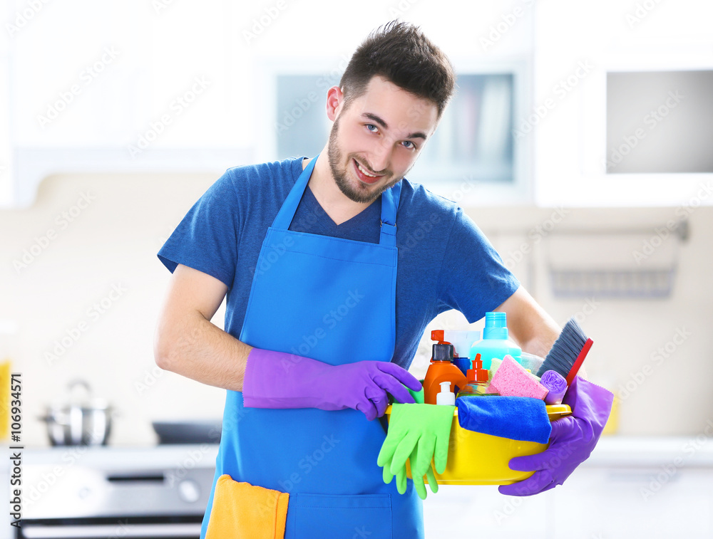 Man holding plastic basin with brushes, gloves and detergents in the kitchen Man holding plastic basin with brushes, gloves and detergents in the kitchen