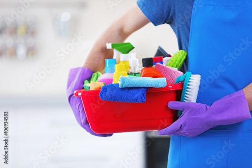 Man holding plastic basin with brushes  gloves and detergents in the kitchen
