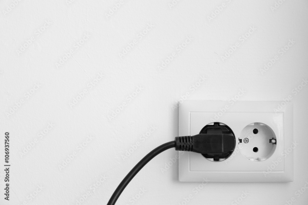 Black power plug into socket against white wall background Black power plug into socket against white wall background