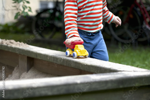 Cropped shot of male toddler pushing toy car around sand pit in garden photo