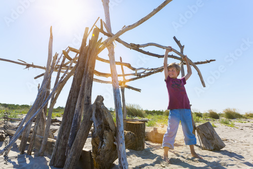 Boy lifting driftwood to construct shelter, Caleri Beach, Veneto, Italy photo