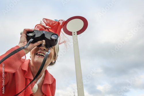 Senior woman at races leaning forward and looking through binoculars photo