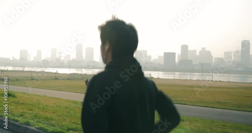 Young Japanese man runs up the hill and celebrates looking over city and river 4K