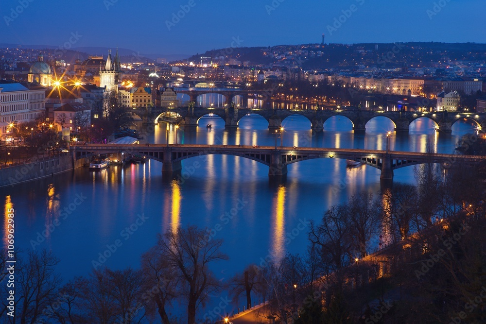 Evening Picture over Prague bridges and riverbank on the Vltava river with Charles bridge included in twilight during the blue hour. Historical downtown of Prague, capital of Czech Republic in Europe.