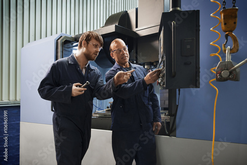 An experienced worker explains the workings of a CNC machine to an apprentice photo