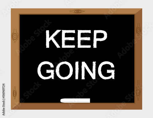 The words Keep Going in white text on a blackboard with a stick of chalk as a reminder to persevere with your ambitions