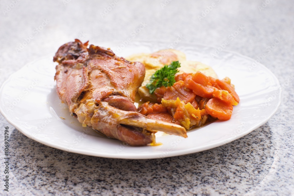 Gourmet roasted rabbit leg with glazed sweet carrot and baked potatoes choped on thin slices. Meal is served on the white simply plate and granit table isolated. Healty and light meal perfect for diet Gourmet roasted rabbit leg with glazed sweet carrot and baked potatoes choped on thin slices. Meal is served on the white simply plate and granit table isolated. Healty and light meal perfect for diet
