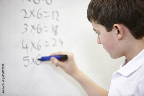 Close up of schoolboy doing multiplication on white board
