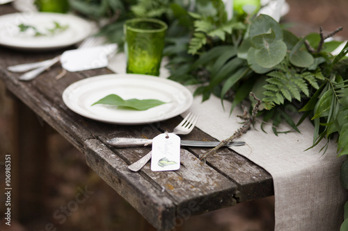 White plate with green leave and silver spoon and fork with blank label on wooden table and linen tablecloth