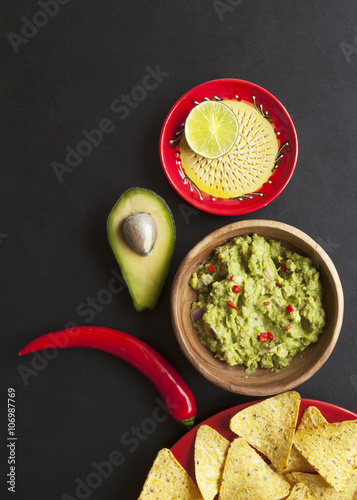 wooden bowl of guacamole and its ingredients on black background from above 