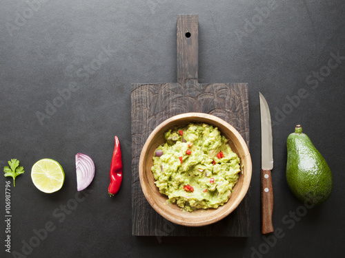 wooden bowl of guacamole and its ingredients on black background from above 