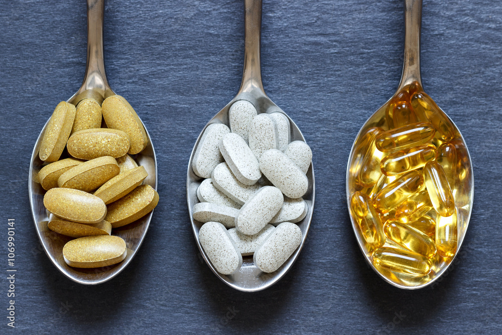 Fotografie Spoons with healthy supplements on a dark stone background
