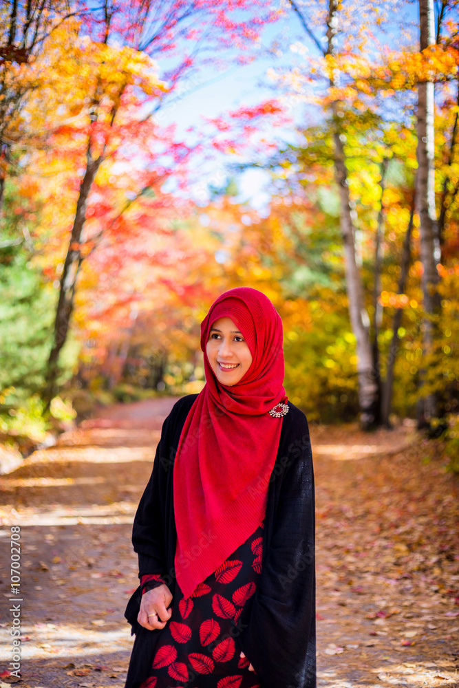 Muslim woman wearing hijab with colourful trees as background during autumn season Muslim woman wearing hijab with colourful trees as background during autumn season