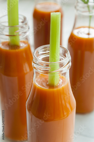 Natural and fresh carrot juice in small bottles with fresh celery on light background