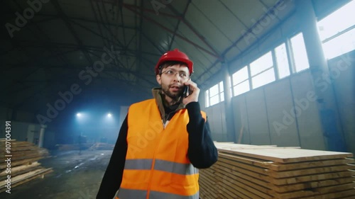 Engineer in helmet goes on a warehouse of building materials, talking on the phone