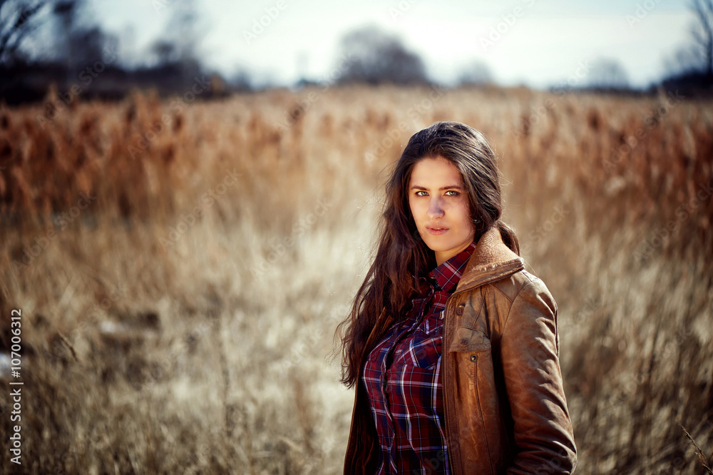 Young beautiful brunette with long curly hair stands in a field. Look direct. Young beautiful brunette with long curly hair stands in a field. Look direct.