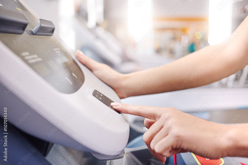 Fototapeta premium woman adjusts the treadmill at the beginning of training, do fitness in the sport club