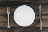 Empty plate with fork and butter knife on wooden background. Top view.