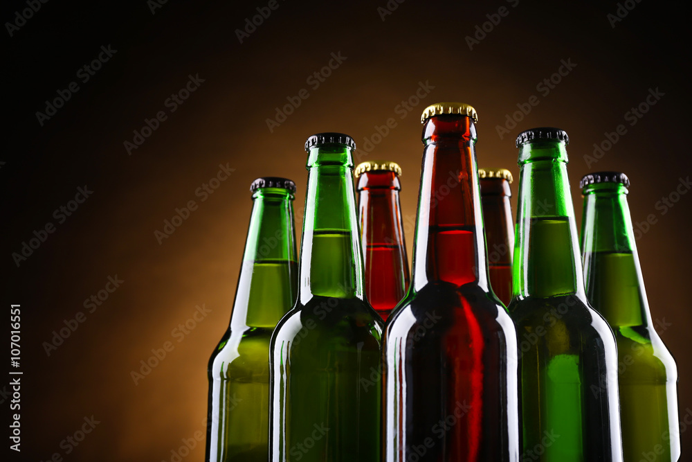 Green and brown glass bottles of beer on dark lighted background, close up
