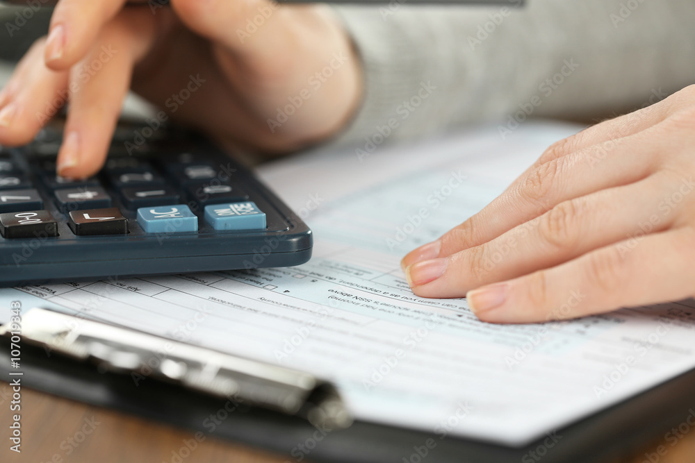 Female hand holding a pen and using calculator while filling in the individual income tax return, close up Female hand holding a pen and using calculator while filling in the individual income tax return, close up