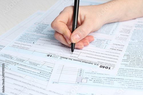 Female hand holding a black pen and filling in the 1040 Individual Income Tax Return Form for 2015 year on the white desk, close up