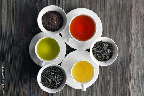 Tea concept. Different kinds of dry tea in ceramic bowls and cups of aromatic tea on wooden background