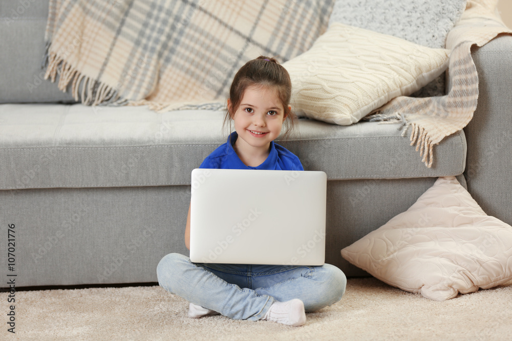Naklejka premium Little girl using laptop on floor indoors
