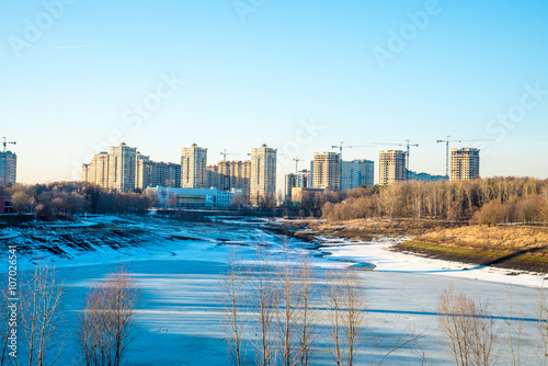 Residential buildings in winter with snow, park and city skyline with skyscrapers, blue sky.