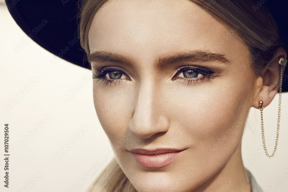 Fototapeta premium Close up of beautiful young blonde woman with black hat. Wearing denim vest. Her hair is tied to ponytail. 