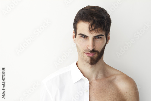 Man half dress in white shirt, standing in front of a camera on a white background with half of his face with scruffy beard and messy hair, the other half has trimmed beards. © anderpe