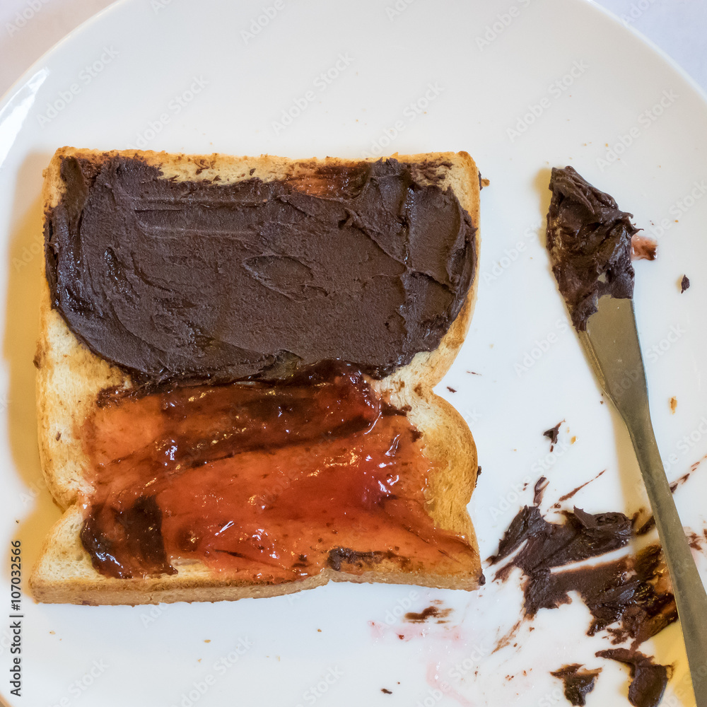 Fototapeta premium The close up of tasty bread toast and strawberry jam with chocolate spread on white plate.