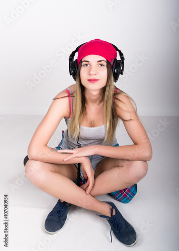 teenager girl in denim shorts and a gray T-shirt and a pink knit hat, tied at the hips plaid shirt. he is sitting on a skateboard and listening to music on headphones