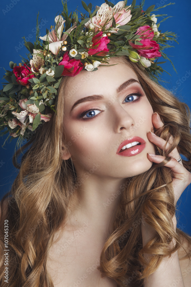 Beautiful young girl with a floral ornament in her hair on a blue background. Woman in wreath of flowers.Beauty Face. Fashion photo.Perfect makeup. Skin care concept.