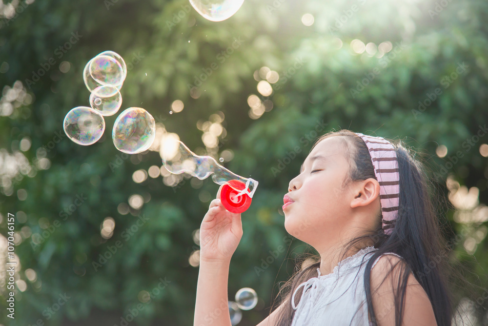 Cute asian girl is blowing a soap bubble